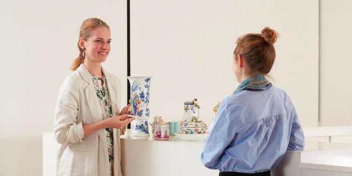 Two women discuss a group of colourful ceramics in a white room.